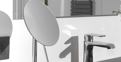 Vrijstaande make-up spiegel op voet naast een chromen kraan en wastafel.